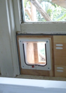 a cat flap installed in a wooden frame, wedged in the opening of a window
